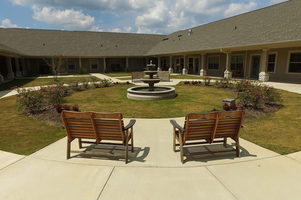 A peaceful courtyard with a central fountain and wooden benches, surrounded by a well-maintained garden.