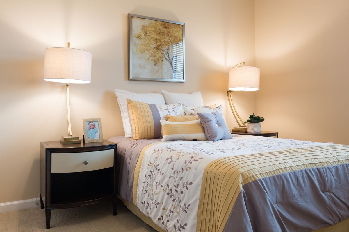A cozy bedroom with elegant decor, featuring a neatly made bed with decorative pillows and warm lighting from bedside lamps.
