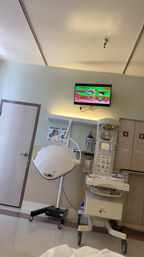 A view of a hospital treatment room with medical equipment and a TV displaying a cartoon.