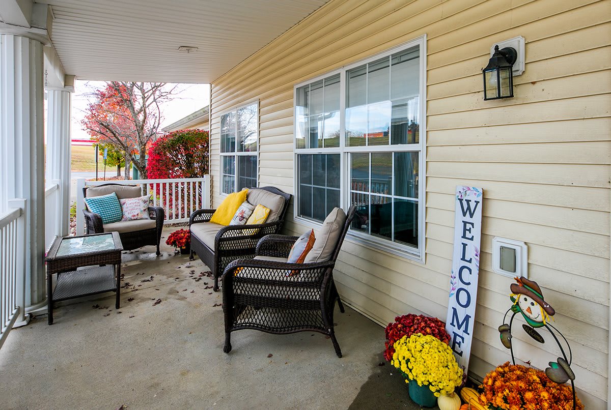 A cozy porch with comfortable seating and vibrant fall decor, including a welcome sign and colorful flowers.