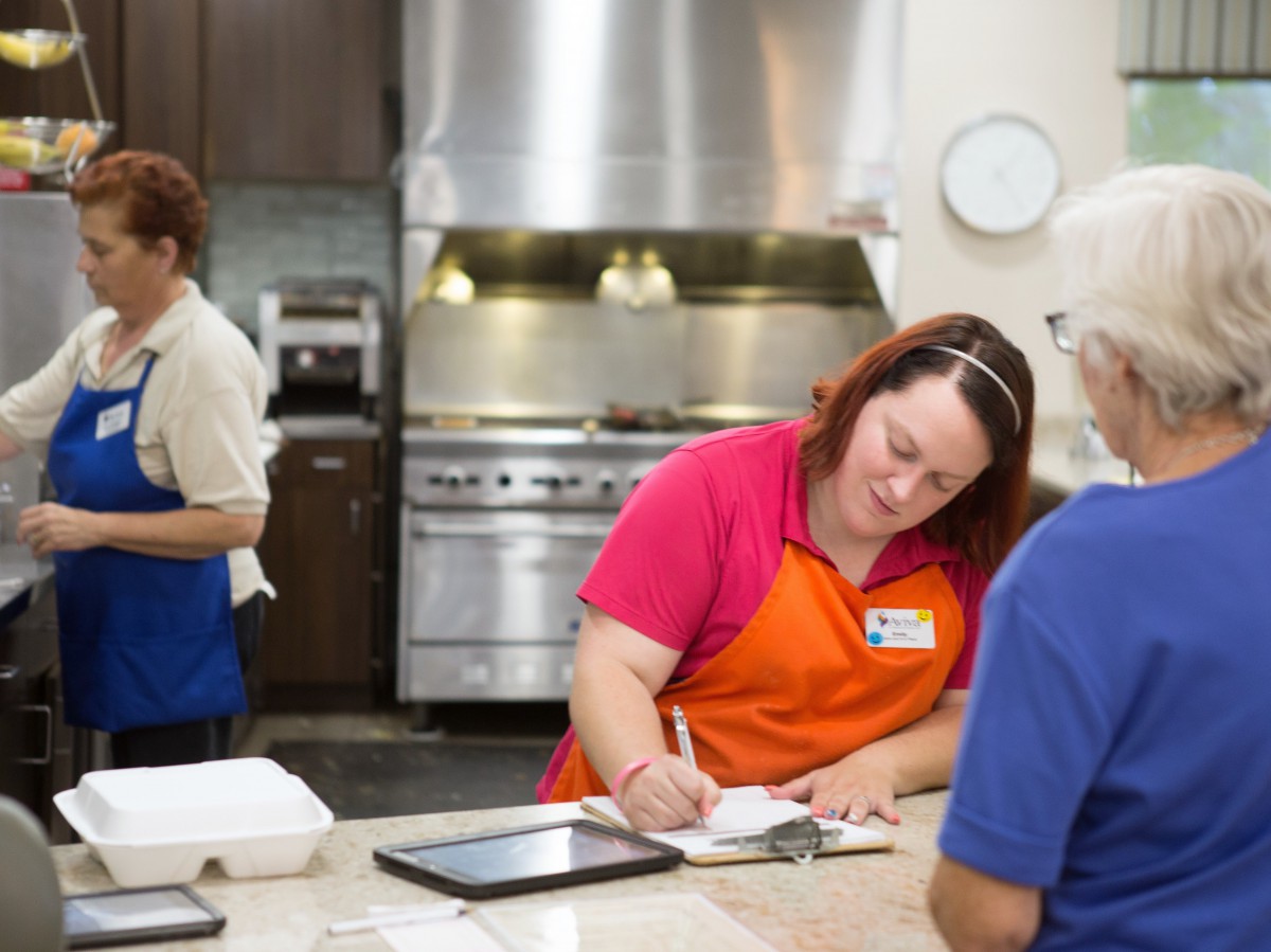 People working in a kitchen, taking orders and preparing food.