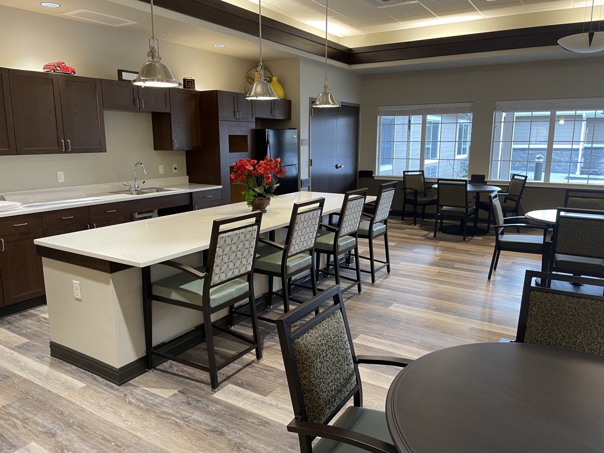 A modern kitchen and dining area with sleek countertops and chairs, illuminated by stylish lighting.
