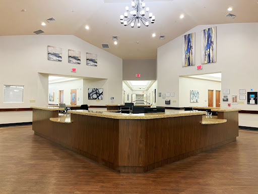 A spacious and modern reception area featuring a wooden counter, elegant chandelier, and contemporary artwork.
