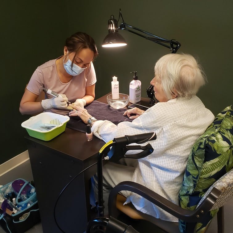 An elderly woman receives a manicure from a nail technician in a cozy setting.