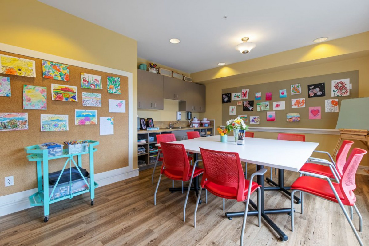A bright and welcoming art classroom with tables, red chairs, and walls adorned with colorful artwork.