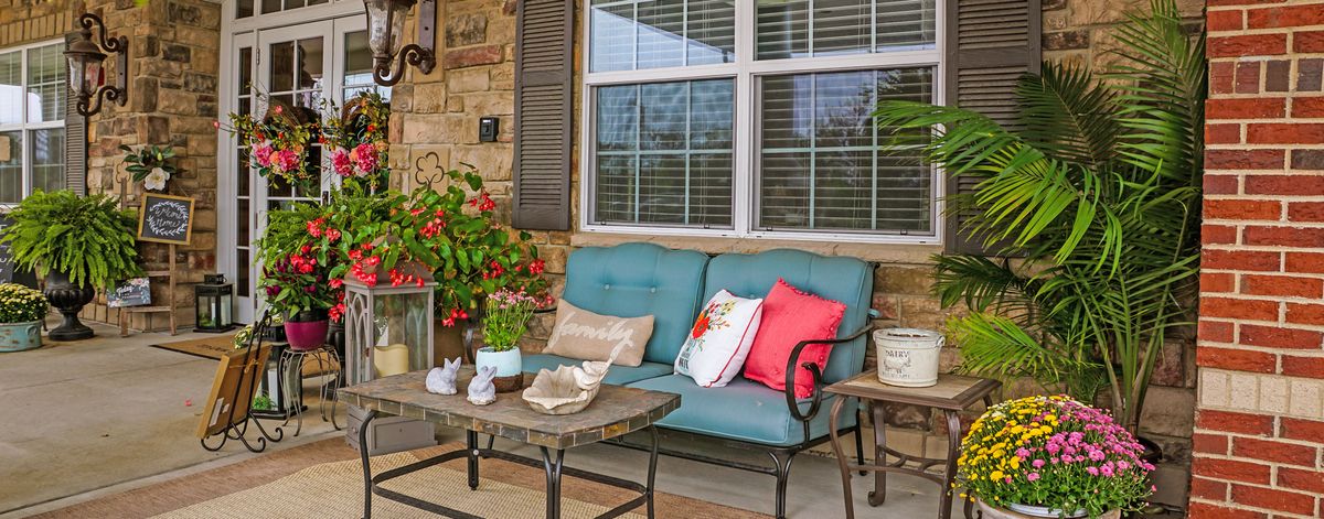 A cozy patio setup with a sofa, colorful cushions, and potted plants.