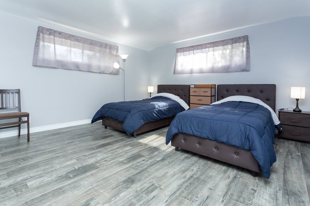 A modern bedroom featuring two beds with blue bedding and wooden flooring.
