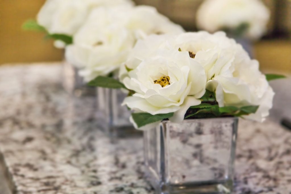 White floral arrangements in square vases on a patterned table.