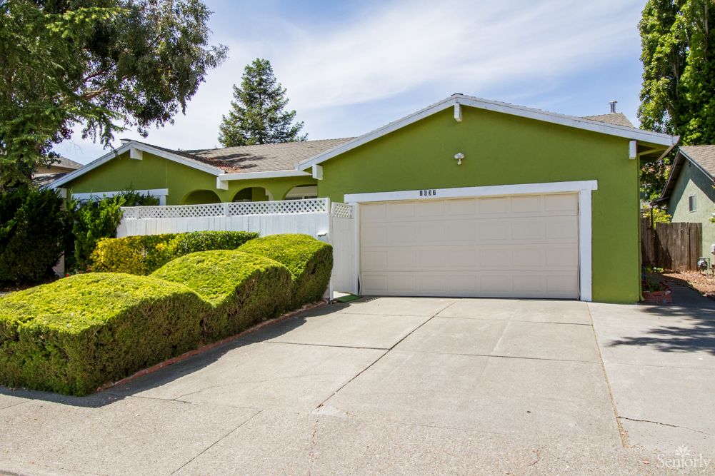 A suburban house with a green exterior and a neatly manicured driveway.