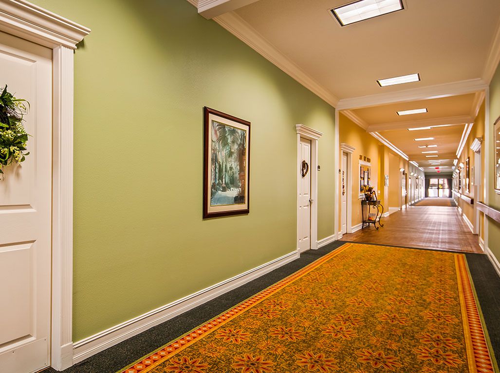 A well-lit hallway featuring green and yellow walls, decorated with framed artwork and patterned carpet.