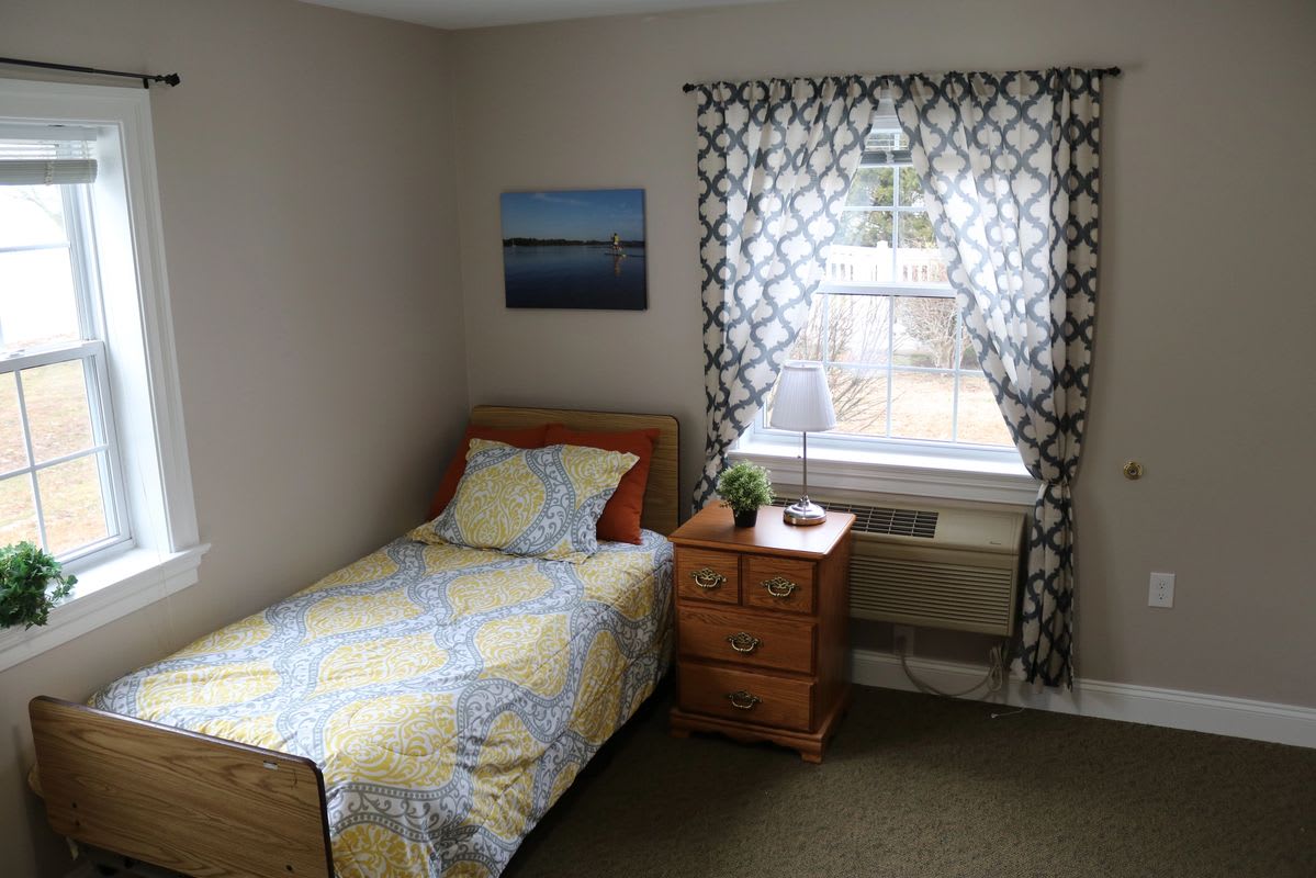 A simple and cozy bedroom with a single bed, nightstand, and a window adorned with patterned curtains.