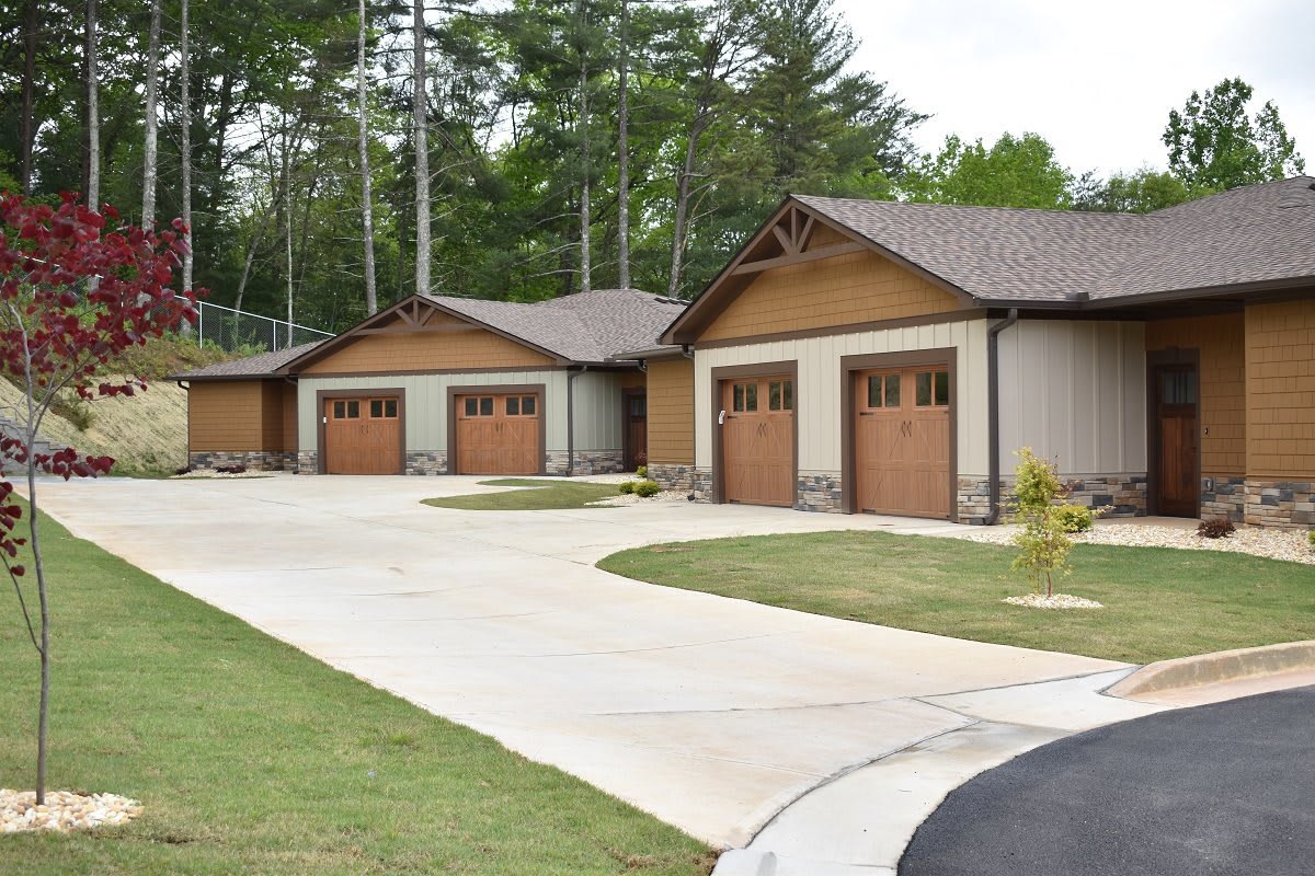 Row of garages with wooden doors in a residential area surrounded by trees.