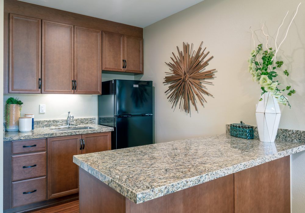 A modern kitchen with wooden cabinets, a granite countertop, and a decorative wall piece.
