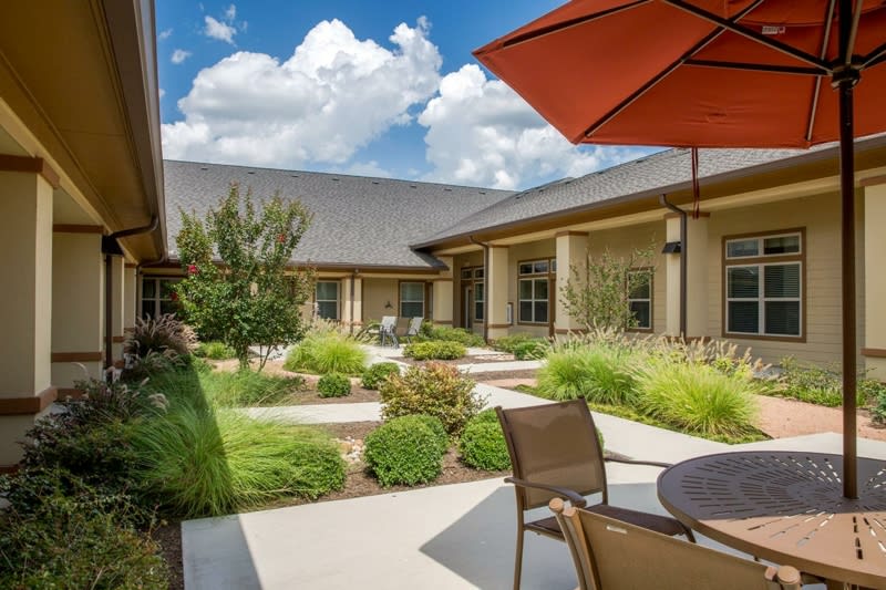 A well-landscaped courtyard with outdoor seating, under a blue sky with clouds.