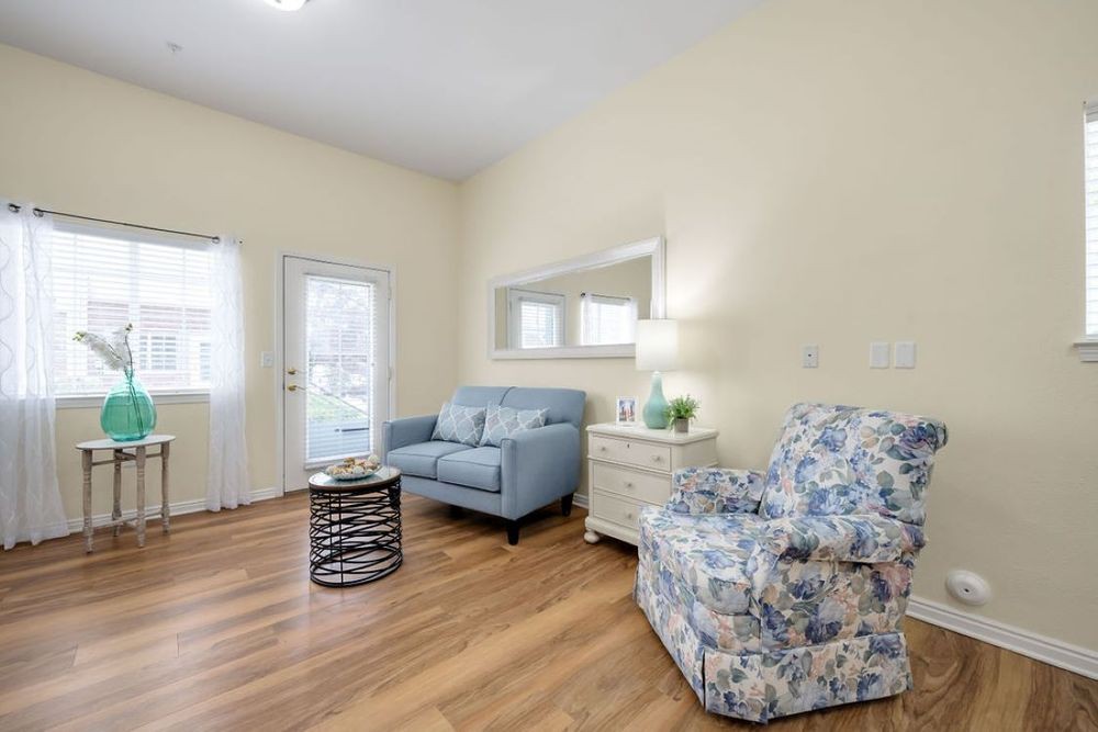 A cozy living room with a blue sofa, floral armchair, and wooden flooring.