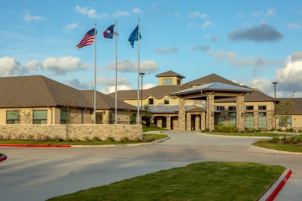 A well-maintained building with a driveway, adorned with three flags waving against a partly cloudy sky.