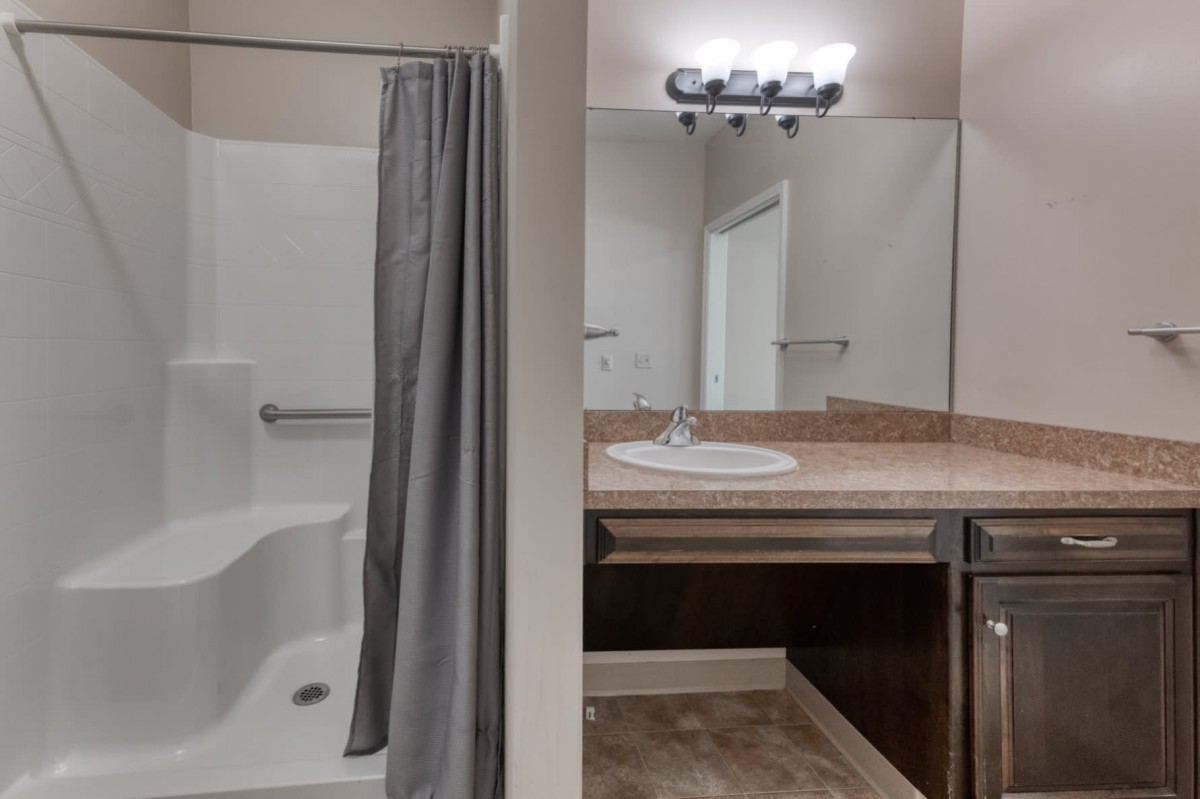 A bathroom with a shower, sink, and large mirror.