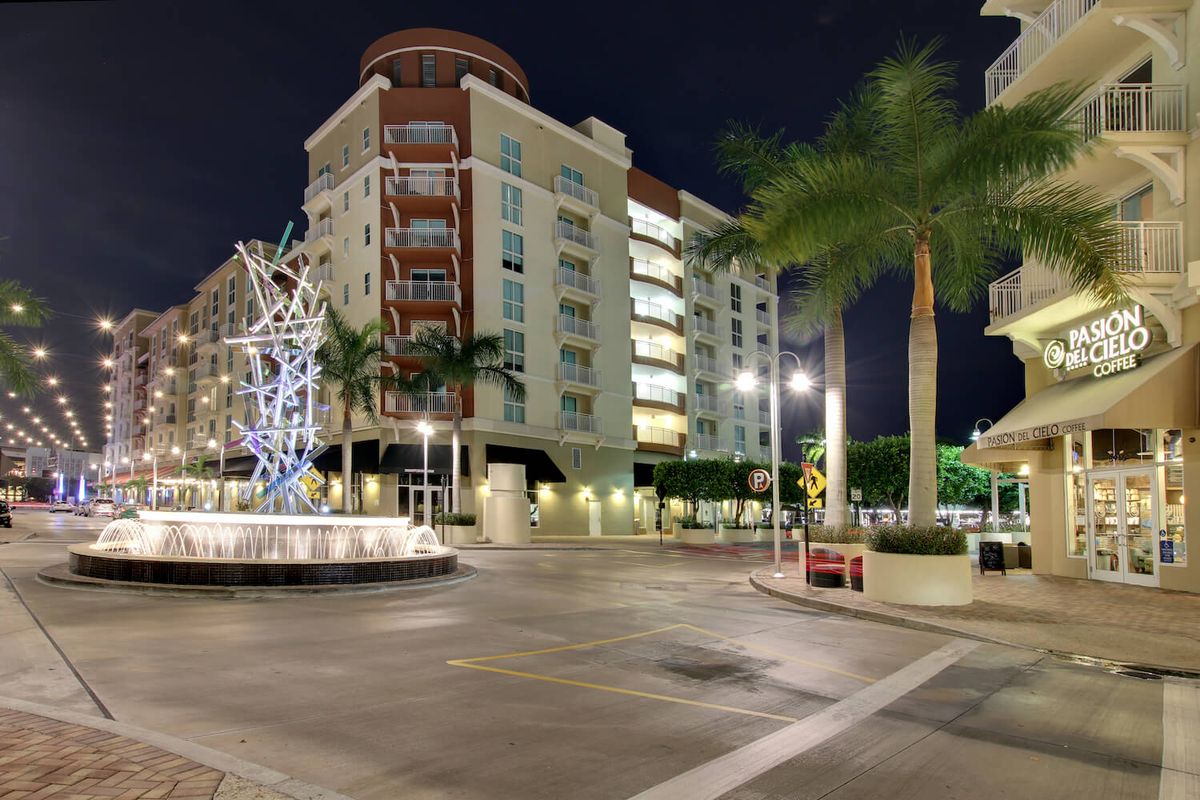 A city street at night with modern buildings and illuminated palm trees.