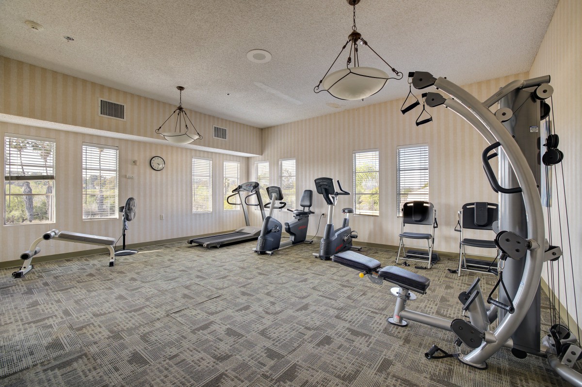 A well-lit gym with various exercise equipment including treadmills and machines.