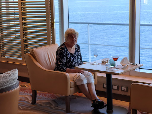 An elderly woman enjoys a peaceful moment at a dining table with an ocean view.