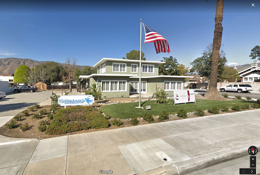 A green building with an American flag in front, surrounded by a landscaped area.