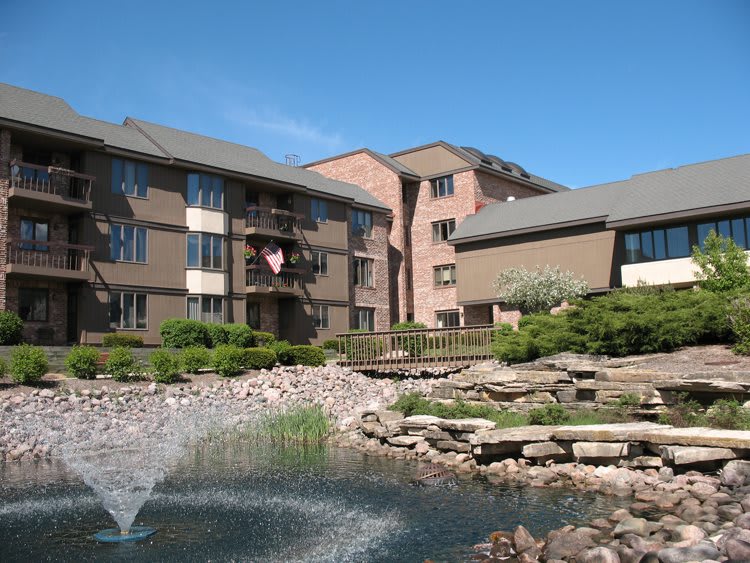 A sunny day view of residential apartment buildings with a landscaped pond and fountain.