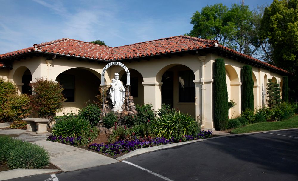 A Mediterranean-style building with an arched entrance and a garden featuring a statue.