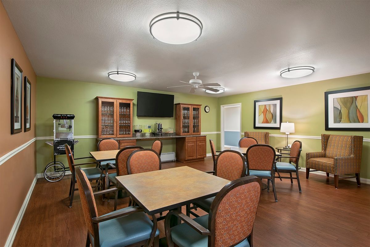 A well-lit dining room with tables, chairs, and a television on the wall.