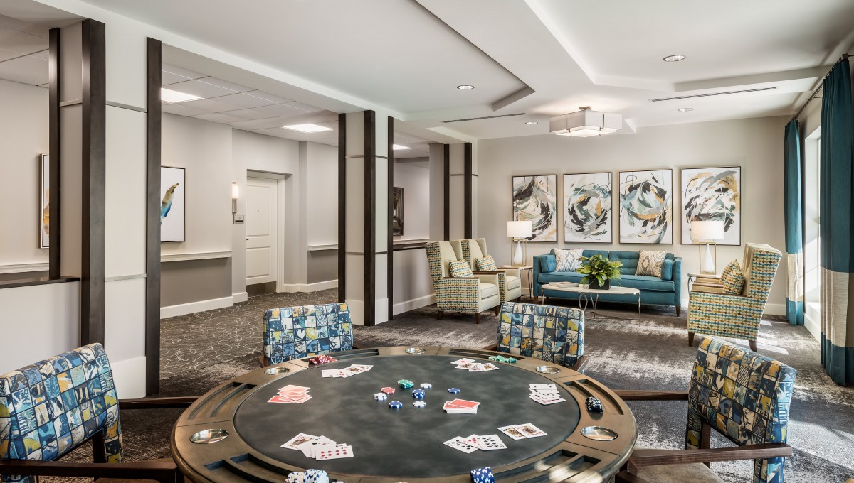 A stylish lounge featuring a poker table with cards and chips, surrounded by comfortable seating and adorned with modern artwork.