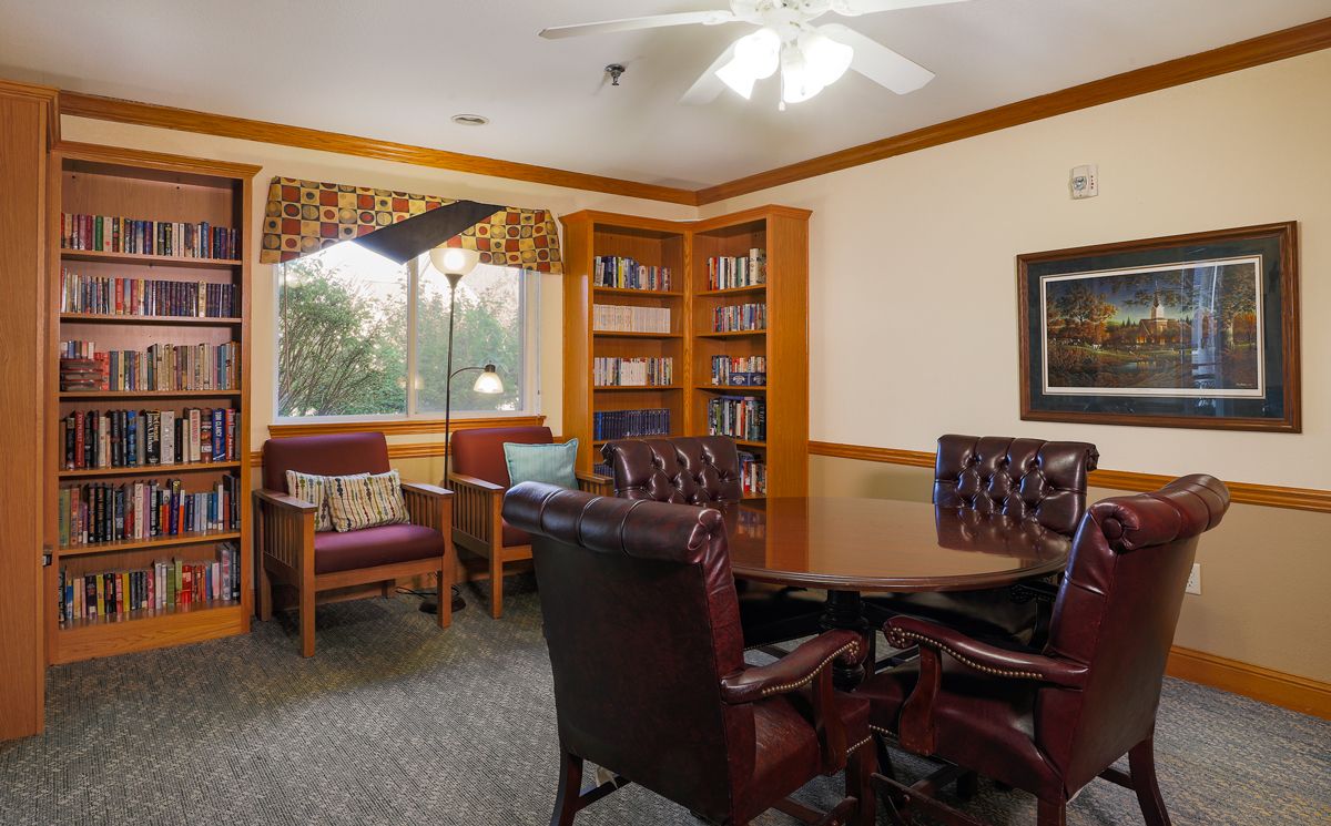 A cozy conference room with a wooden meeting table, leather chairs, and a bookshelf by the window.
