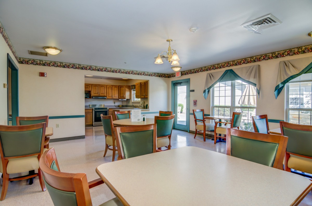 A well-lit dining area with tables and chairs adjacent to a kitchen.