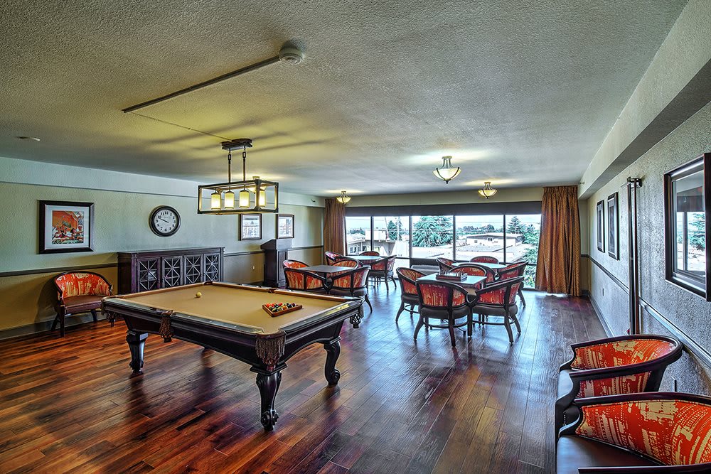 A spacious game room featuring a pool table and dining tables, with large windows and elegant chandeliers.