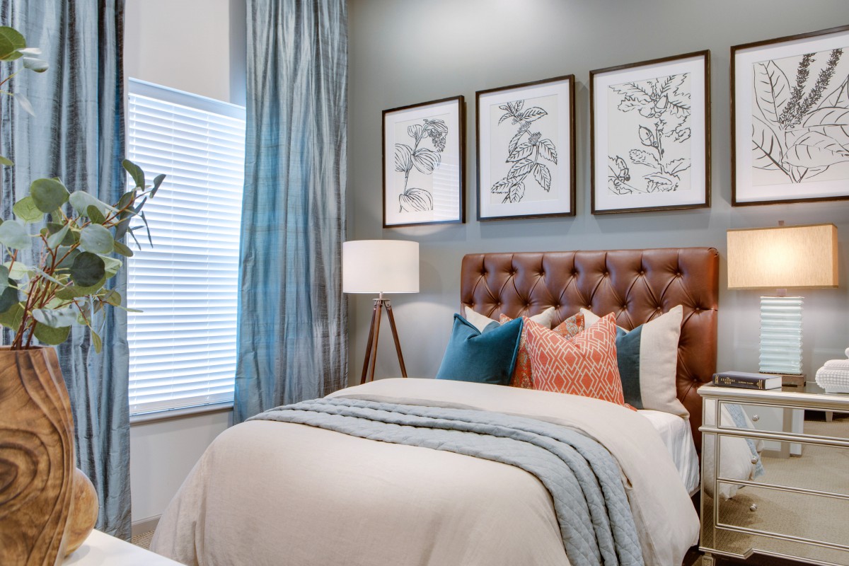 A cozy bedroom with a tufted headboard, framed botanical artwork, and layered bedding featuring various textured pillows.