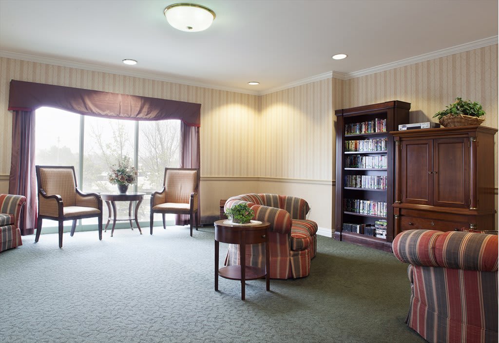 A cozy living room with comfortable chairs, a bookshelf, and a large window letting in natural light.
