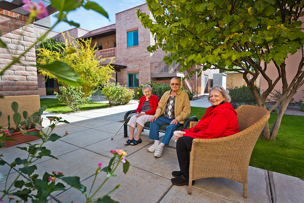 A group of seniors sitting and enjoying the outdoor garden area in a community setting.