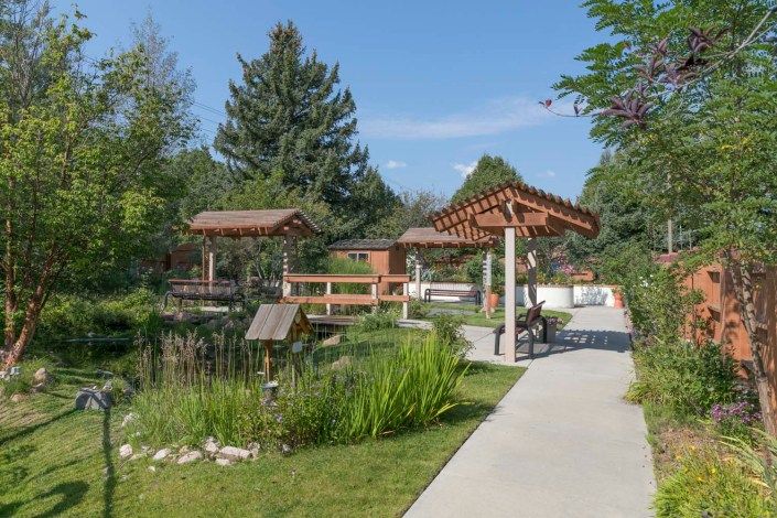 A serene garden with a concrete pathway, surrounded by lush greenery and wooden gazebos.
