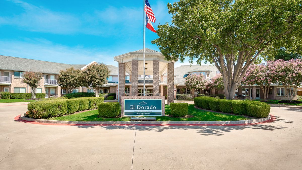 The entrance of a building with an American flag, surrounded by trees and bushes.