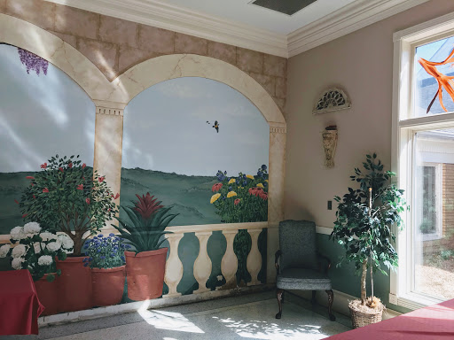 A beautifully decorated interior space featuring a mural of a landscape, potted plants, and elegant furnishings.