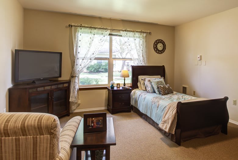 A cozy bedroom with a single bed, television, and a window providing natural light.