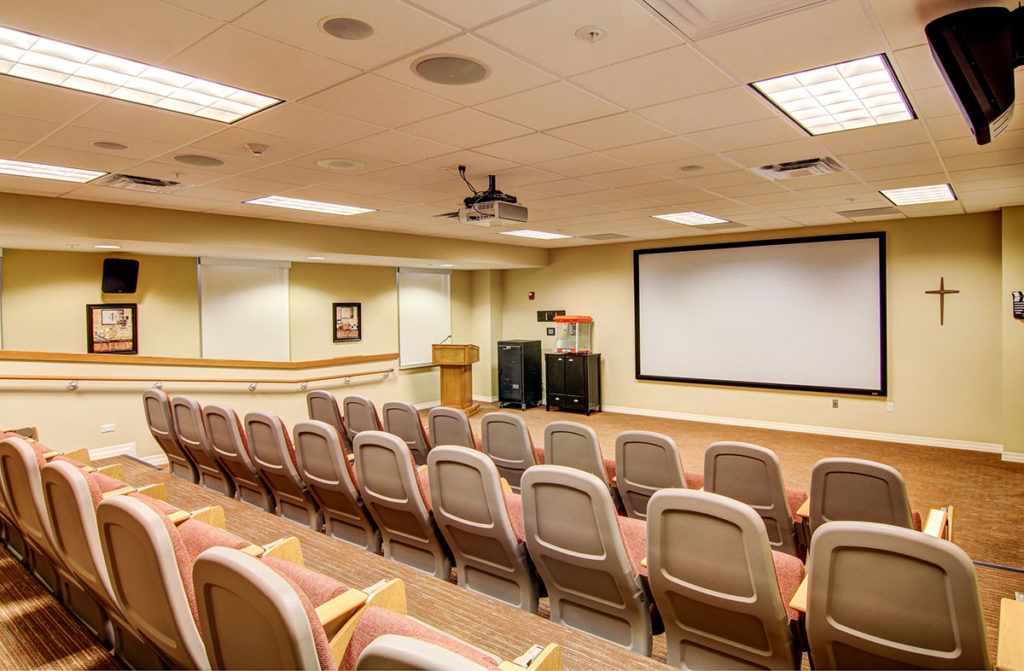 An empty conference room with rows of seating facing a large projector screen.