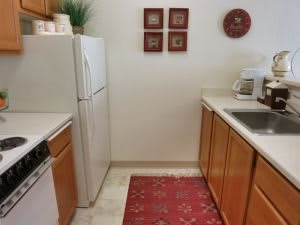 A small kitchen featuring wooden cabinets, a refrigerator, microwave, dishwasher, and decorative touches.