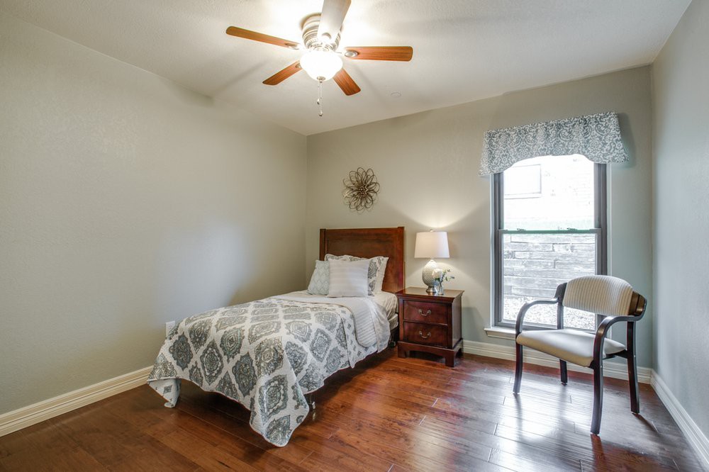 A cozy bedroom with a single bed, wooden floors, and a large window allowing natural light.
