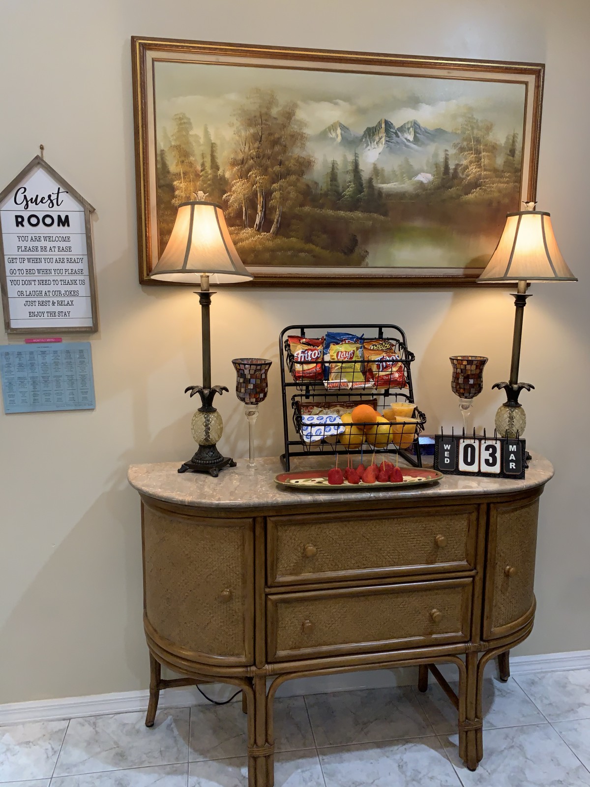 A decorated table featuring snacks, two lamps, and a landscape painting.