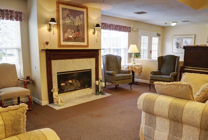 A cozy living room features a fireplace, armchairs, and natural light through the windows.