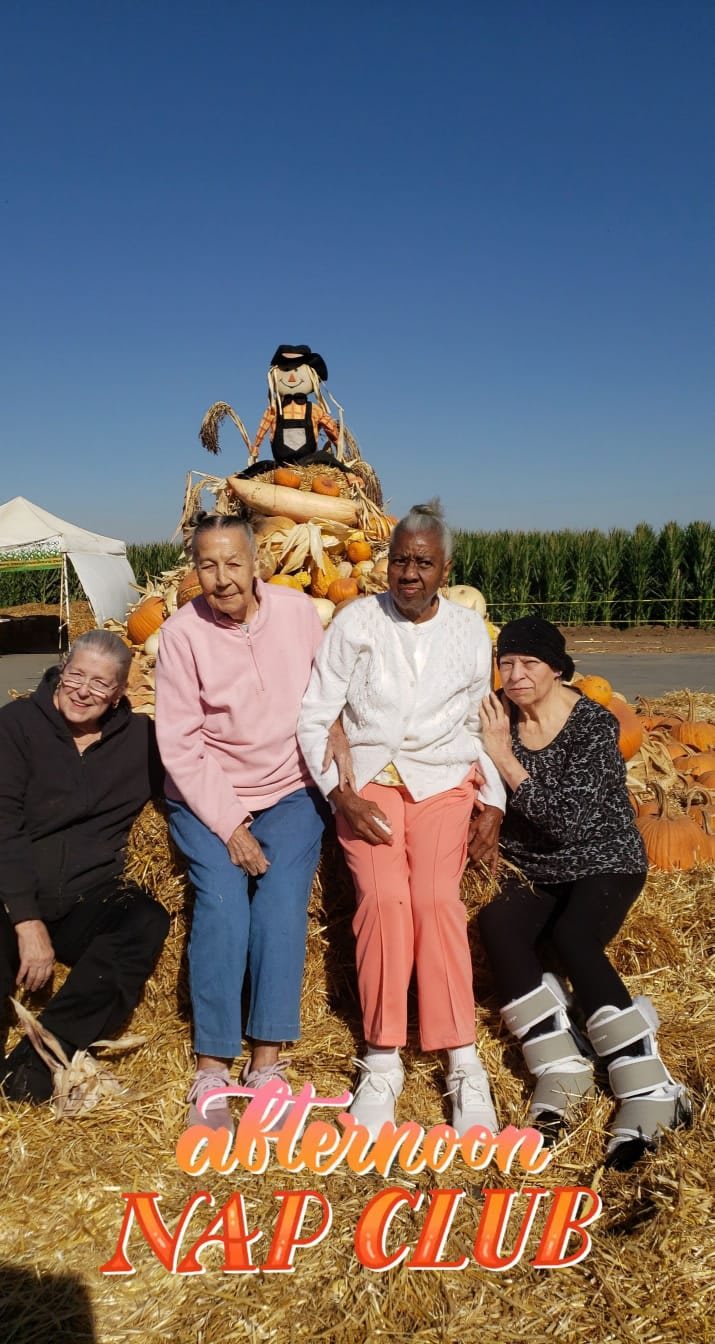 A group of four people pose together in front of a festive autumn display with pumpkins and hay bales under a clear blue sky.
