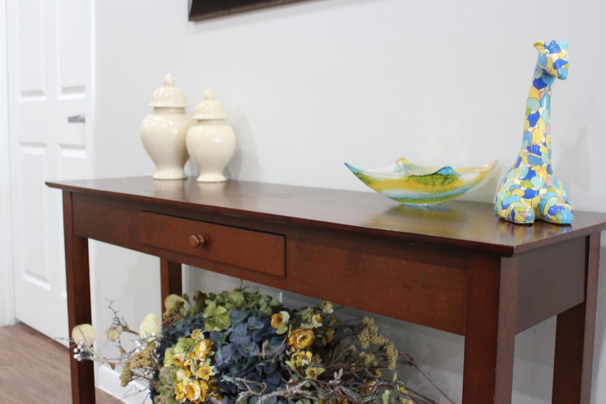 A wooden console table decorated with vases and a glass dish, with a floral arrangement below.