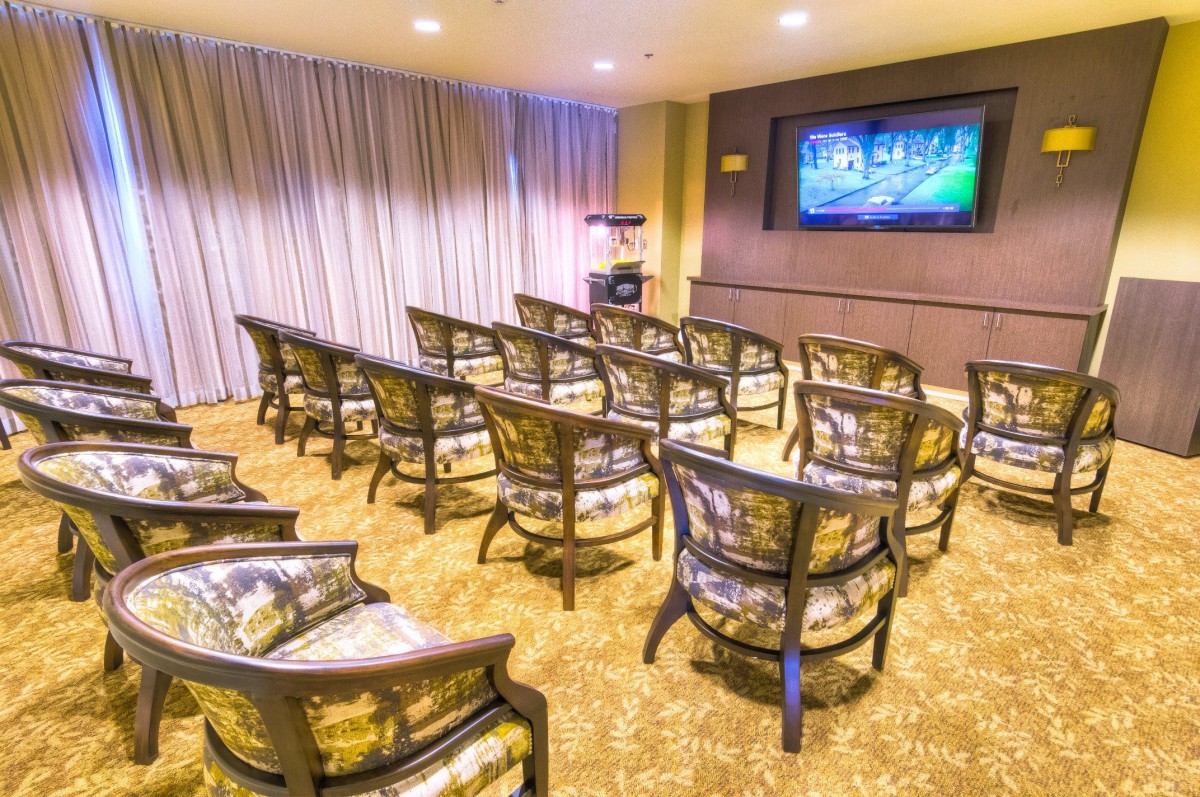 A well-lit conference room with multiple rows of upholstered chairs facing a projector screen.