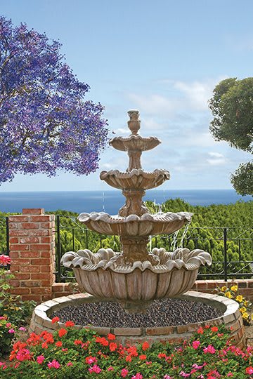 A beautiful three-tiered fountain in a garden with a stunning sea view.