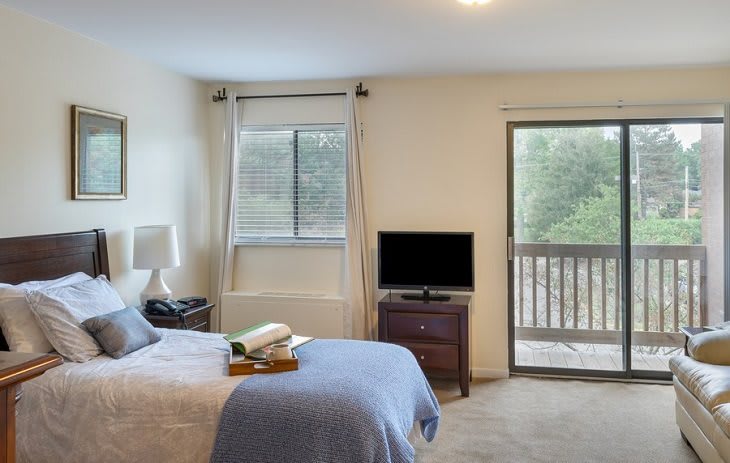 A cozy bedroom with a bed, television, window, and balcony access.