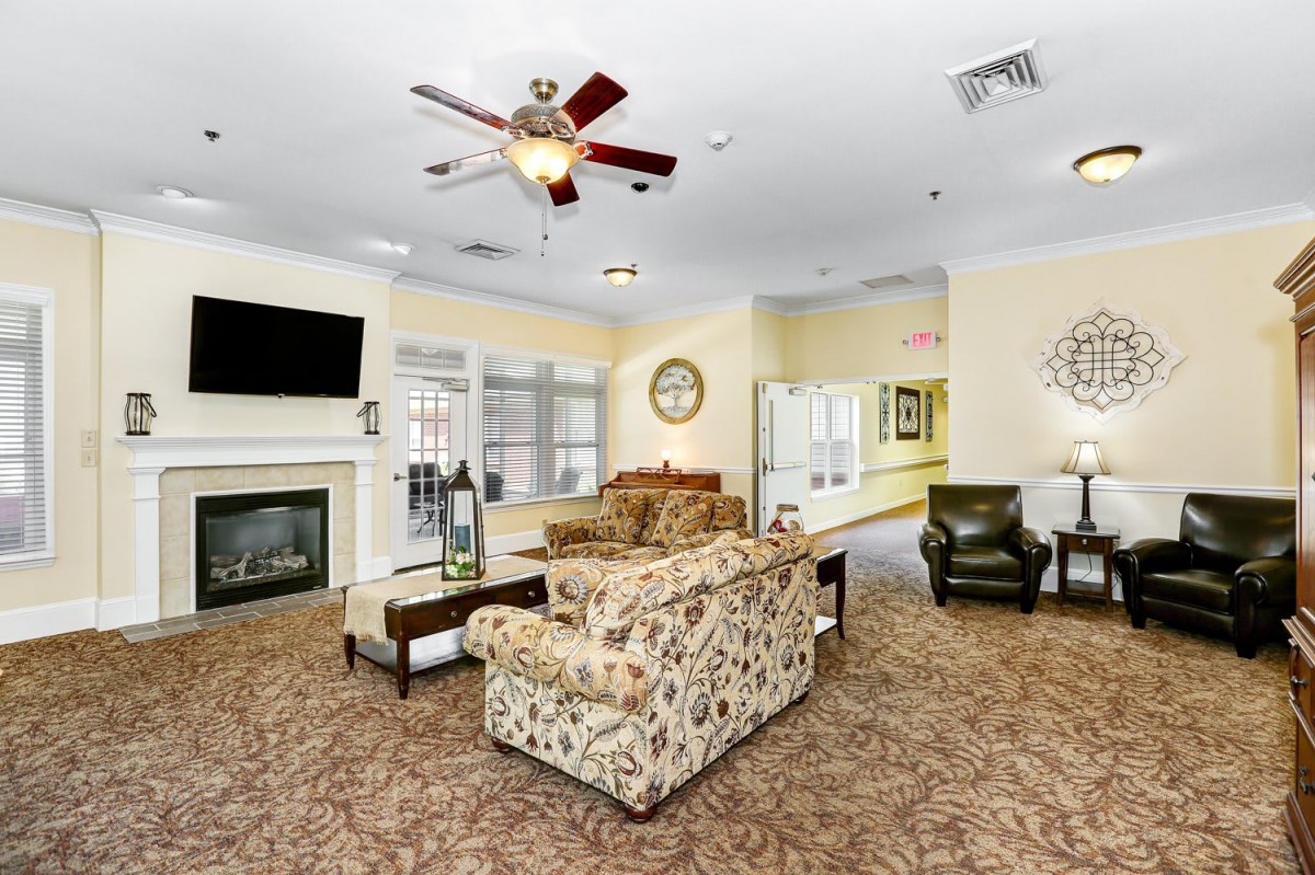 A cozy living room with a fireplace, sofa, armchairs, and a ceiling fan.